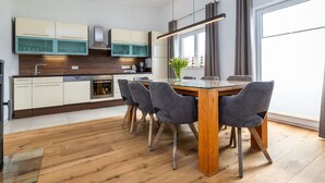 A modern kitchen with wooden cabinets, a built-in oven, and a dining area with a glass table and grey chairs.