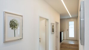 A clean, modern hallway with white walls, framed artwork, and a staircase leading to a door with a window.