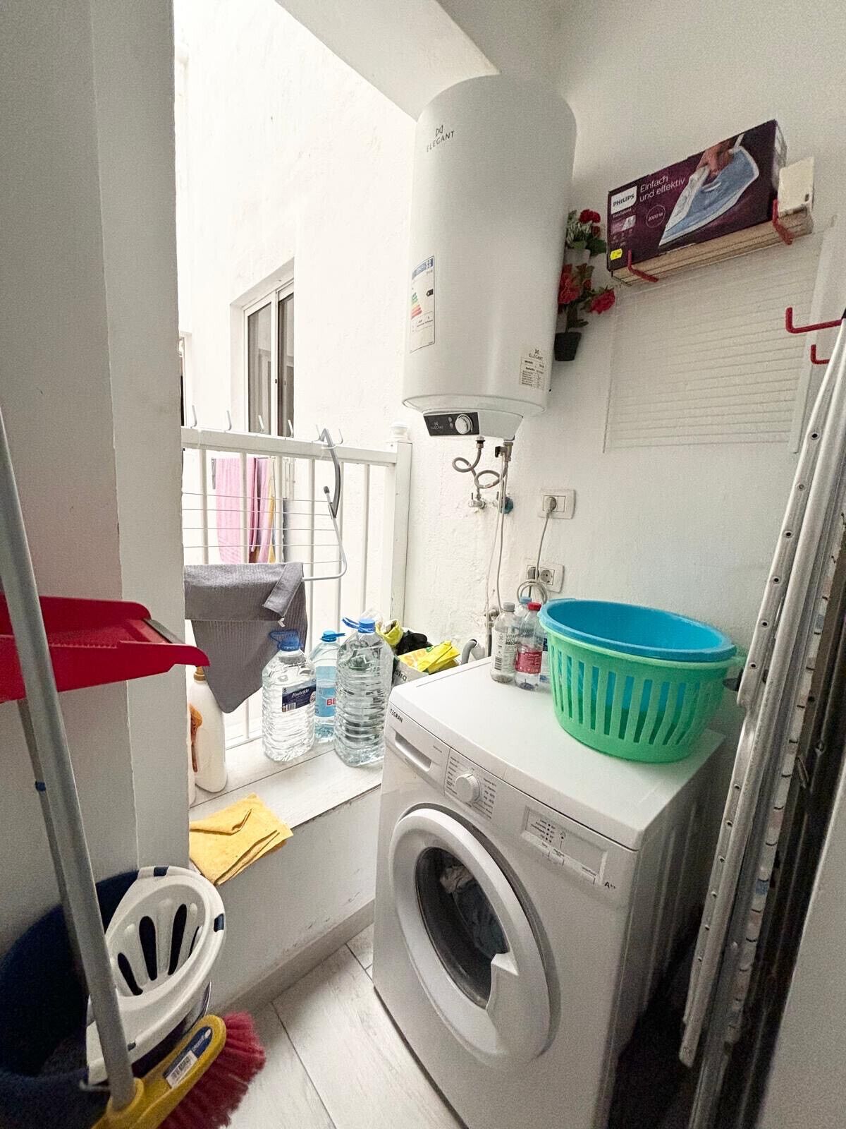 Een kleine wasruimte met een wasmachine, een boiler en een droogrek.