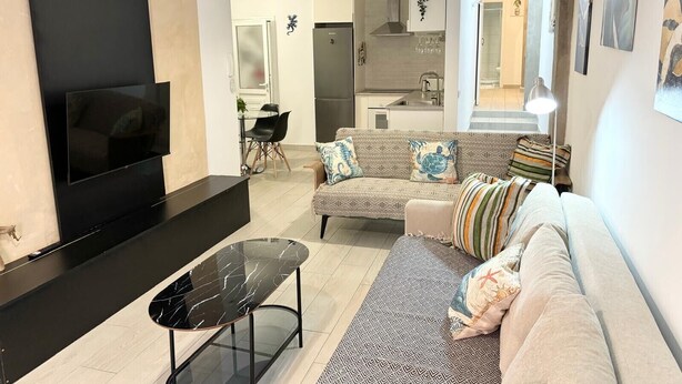 A modern living room with a black TV, a marble coffee table, and a patterned sofa.
