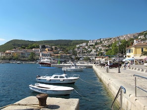 A harbor with boats docked, a waterfront promenade, and a hillside town in the background.