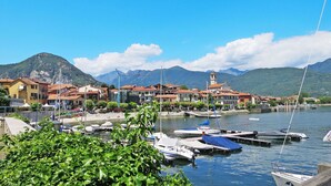 Uma marina com barcos atracados, cercada por edifícios com telhados vermelhos, e montanhas ao fundo.