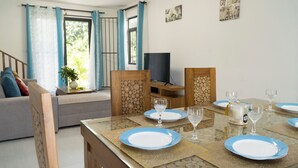 Un coin repas avec une table dressée pour quatre personnes, un canapé et un téléviseur en arrière-plan.