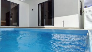 Une piscine à l’eau d’un bleu cristallin, entourée de murs blancs et dotée de grandes fenêtres.