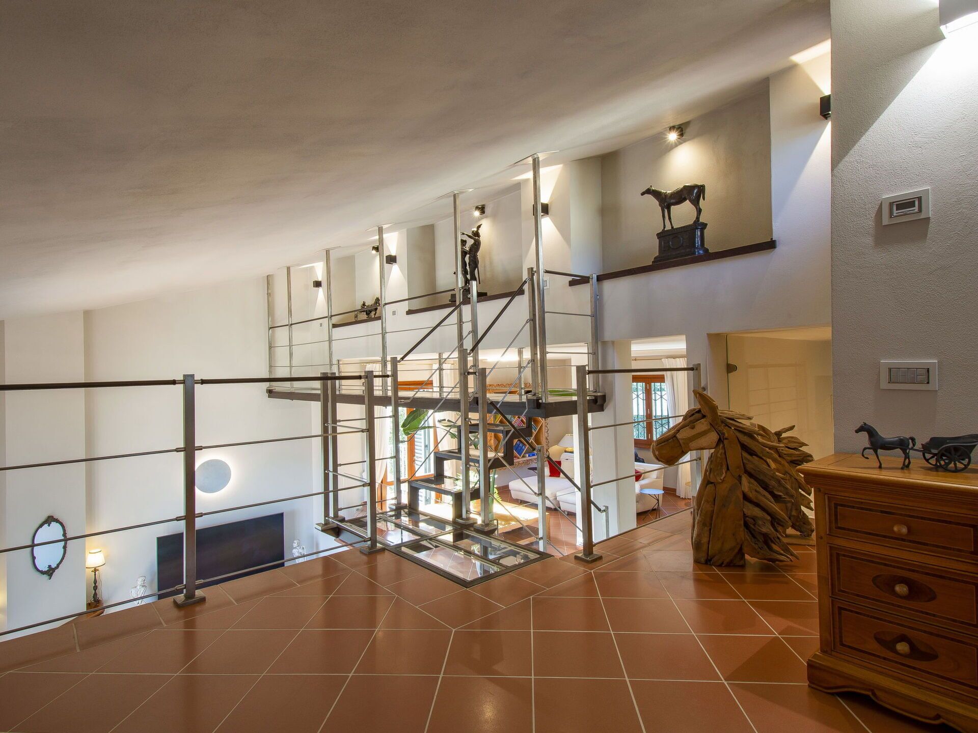 A spacious interior with a high ceiling, a metal staircase, and a wooden cabinet.