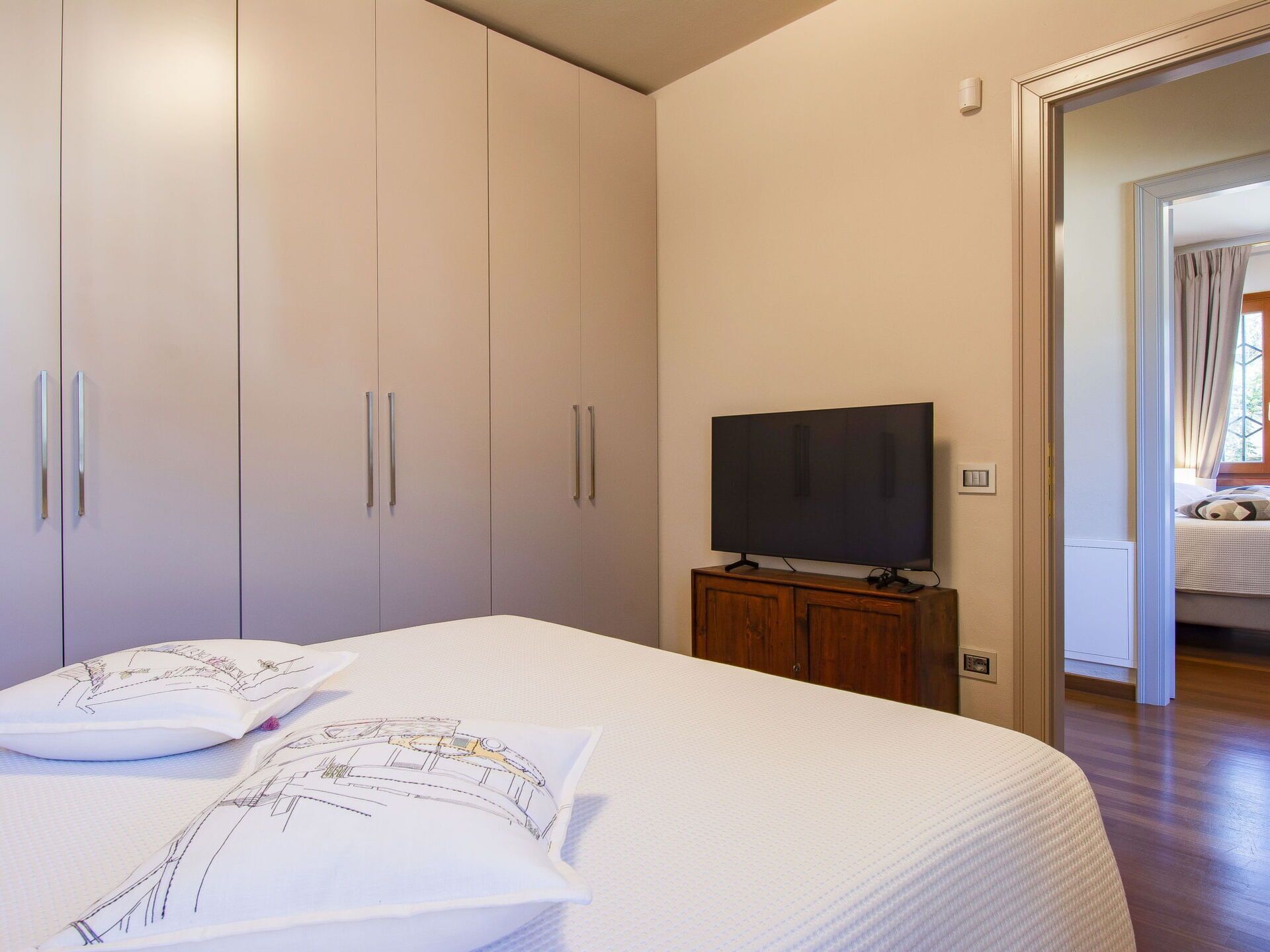 A bedroom with a large bed, a television on a wooden stand, and a wardrobe with sliding doors.
