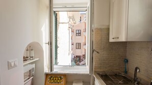 Uma cozinha compacta com janela, pia e uma pequena prateleira com utensílios de cozinha.
