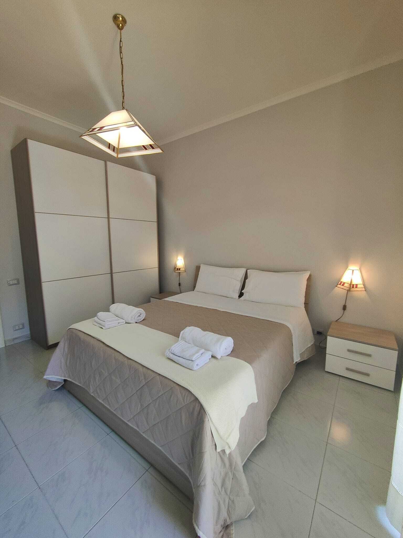 A bedroom with a large bed, two bedside lamps, a wardrobe, and a nightstand.