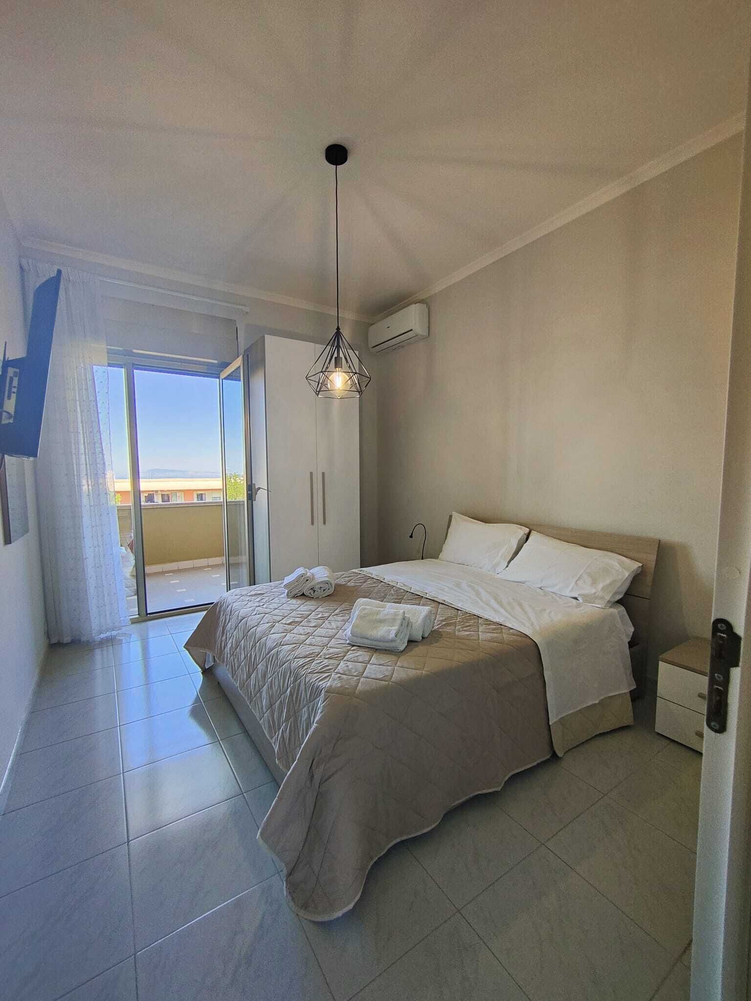 Et soveværelse med seng, et natbord, en hængende lampe og en skydedør til en balkon.