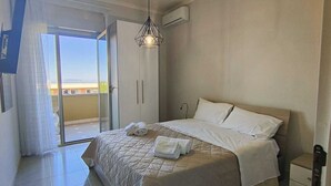 Camera da letto con un letto, un comodino, una lampada a sospensione e una porta a vetri scorrevoli che dà su un balcone.