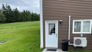 Ett hus med en ytterdörr, en liten veranda, en svart soptunna och en luftkonditioneringsanläggning.