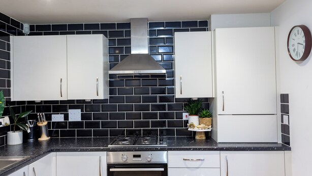 A modern kitchen with white cabinets, black tiled backsplash, stainless steel appliances, and a clock on the wall. - Modern Main Door Flat Edinburgh City Center (Edinburgh)