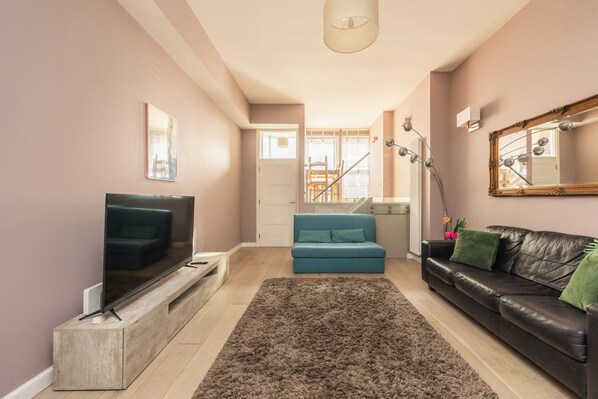 A living room with a flat-screen TV, a blue sofa, a black leather sofa, a brown shag rug, and a large mirror.