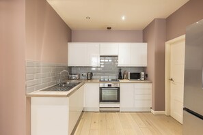 A compact kitchen with white cabinets, a stainless steel sink, a microwave, a toaster, and an oven.