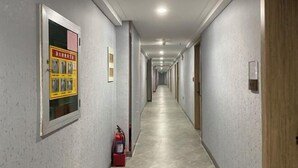 Un long couloir étroit aux murs de couleur claire et au sol carrelé. Un extincteur est fixé au mur, près de l’entrée.