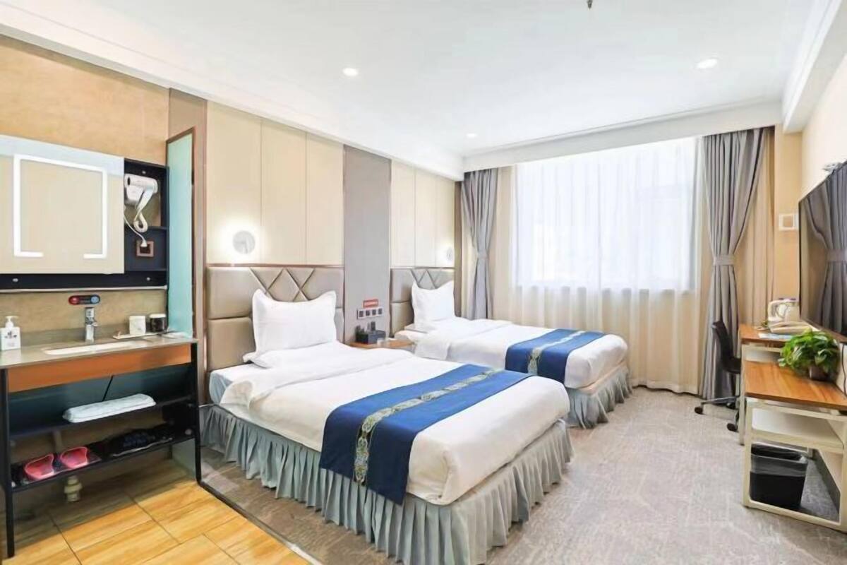 Ett hotellrum med två sängar, ett skrivbord, en stol, en spegel och ett fönster med gardiner.