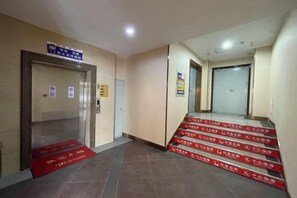 Entrada de un hotel con alfombra roja que lleva a una escalera y un ascensor.