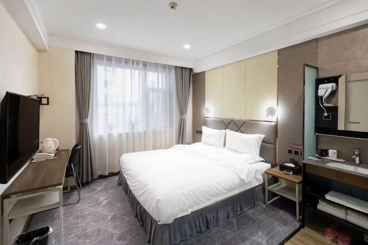 Ett hotellrum med en säng, ett skrivbord, en tv, ett badrum och ett fönster med gardiner.