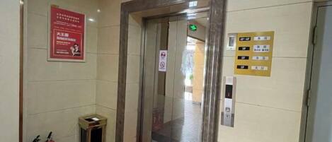 An elevator with emergency exit signs, a fire extinguisher, and a red carpet leading to it.
