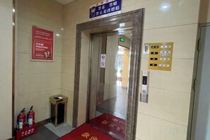 An elevator with emergency exit signs, a fire extinguisher, and a red carpet leading to it.
