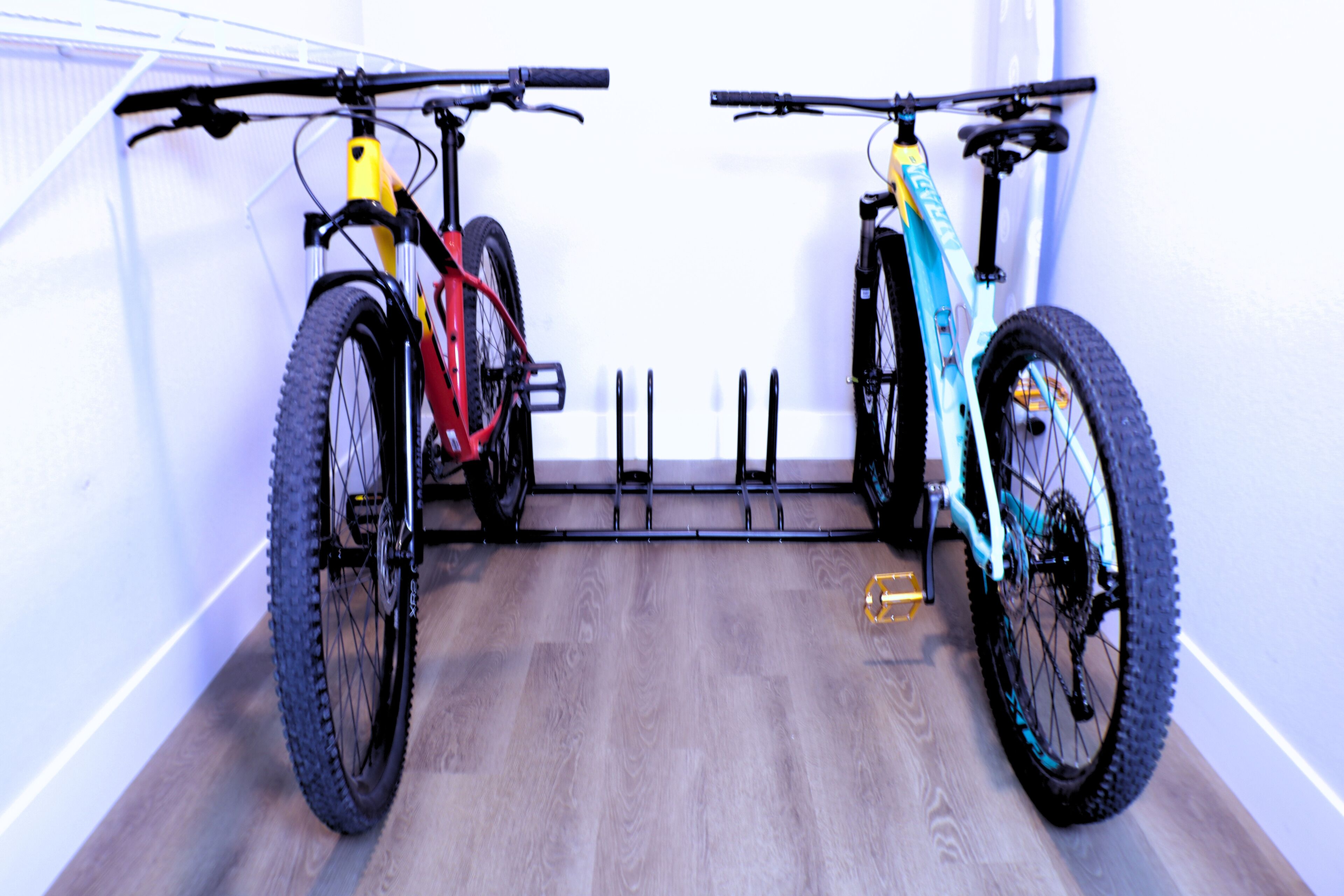 Two bicycles mounted on a wall-mounted rack in a room with wooden flooring.