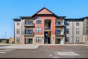 A multi-story building with a central entrance, balconies, and a parking lot in front.