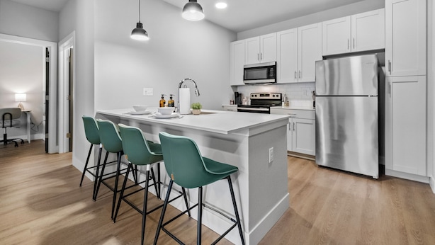A modern kitchen with white cabinets, a stainless steel refrigerator, and a central island with bar stools. - King 1BR + pool near the Walmart NWA Championship (Rogers)