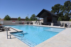 A swimming pool with a lifeguard station, lounge chairs, and a covered seating area.