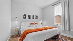 A bedroom with a bed, a nightstand, a lamp, a window with curtains, and abstract wall art. - King 1BR + pool near the Walmart NWA Championship (Rogers)