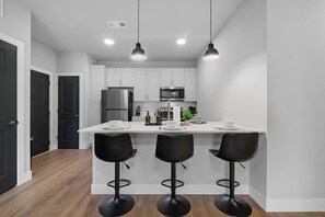 Une cuisine moderne avec des meubles blancs, un îlot central doté de tabourets, un réfrigérateur, un four à micro-ondes et un évier.