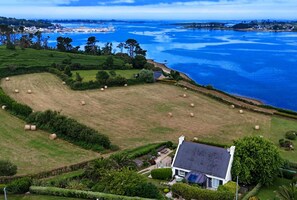 A coastal property with a large field, a house with a sloped roof, and a view of the sea.