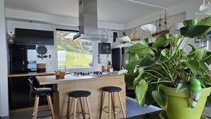 A modern kitchen with a central island, bar stools, a large green plant, and a ship model on the wall. - Beautiful house with incredible sea view over Aber Wrach (Landéda)