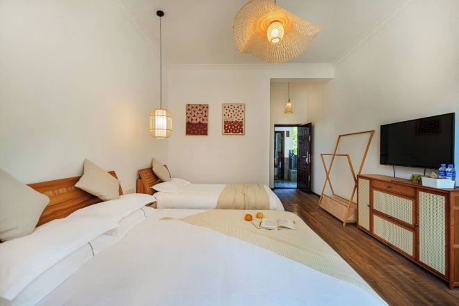 A hotel room with two beds, a television, a wooden cabinet, and a woven ceiling light fixture.