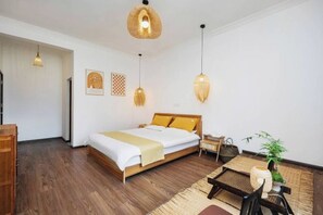 Une chambre à coucher avec un lit en bois, une petite table, une chaise, un luminaire suspendu et une étagère fixée au mur.