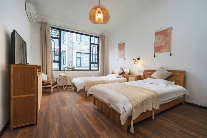 A hotel room with two beds, a desk, a chair, a wardrobe, and a large window.