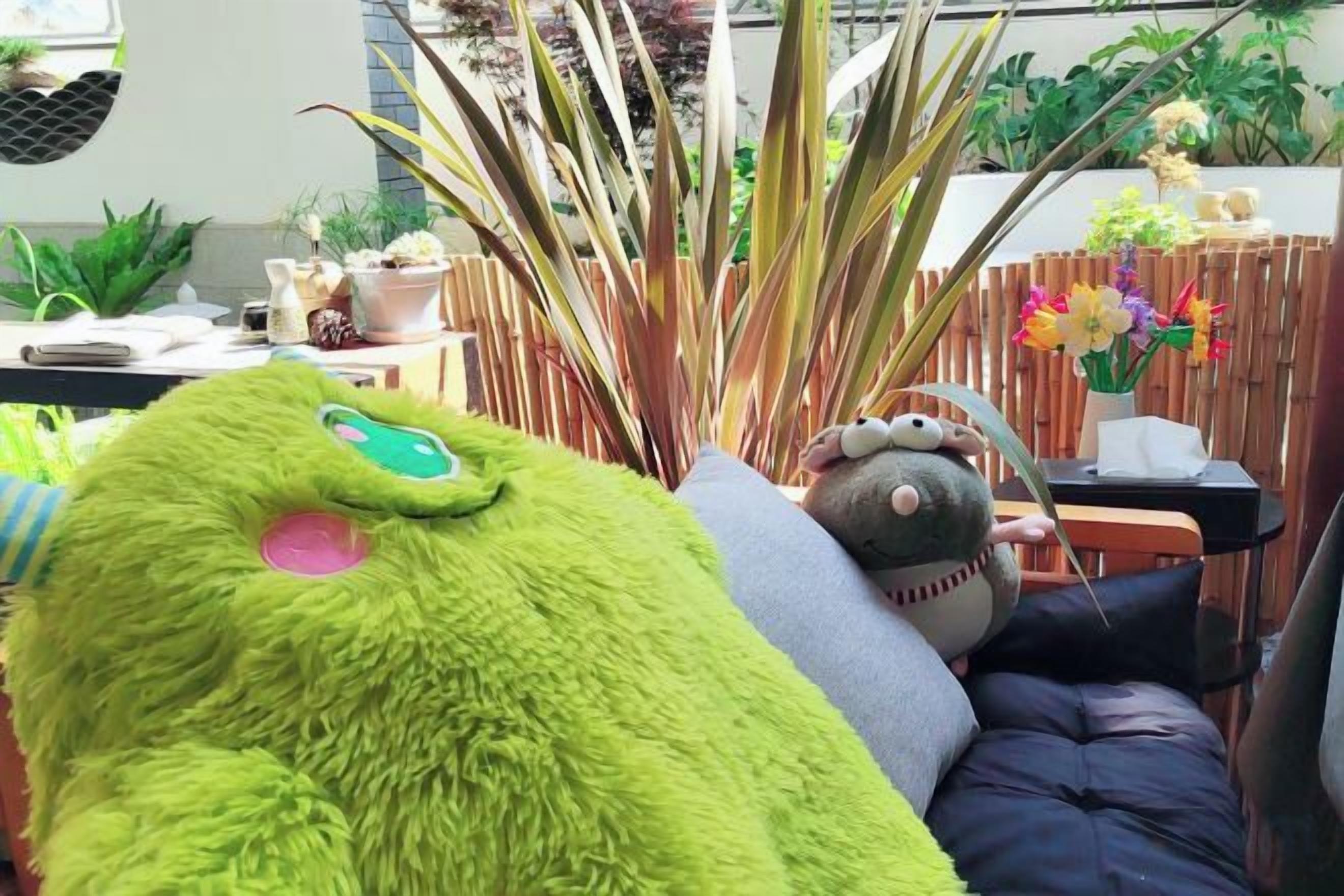 Una habitación con un gran peluche verde, un sofá y una valla de madera.
