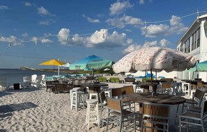 A beachside restaurant with outdoor seating, umbrellas, and a view of the sea.