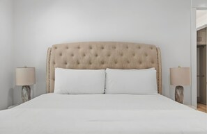 A bed with a tufted headboard, two bedside tables with lamps, and a plain wall.