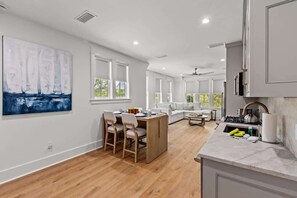 A modern kitchen with a dining area, wooden flooring, and large windows.