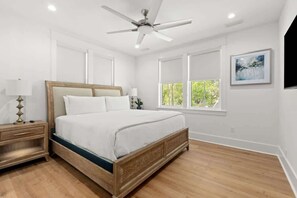 Quarto com cama de madeira, mesa de cabeceira, ventilador de teto e janela com vista para vegetação.