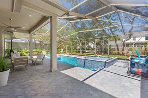 A covered outdoor swimming pool area with a patio, seating, and a grill.
