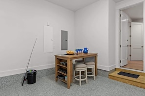 Quarto pequeno e limpo com uma mesa de madeira, dois banquinhos, uma vara de pesca e um balde.