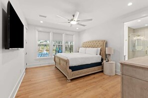 Quarto com cama grande, ventilador de teto, TV e vista para uma piscina pela janela.
