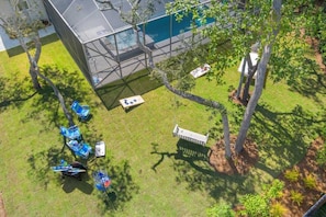 Vista aérea de um edifício moderno com fachada de vidro, piscina e gramado bem cuidado com árvores e mobiliário de exterior.