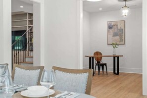 A dining area with a table set for two, a staircase in the background, and a painting on the wall.