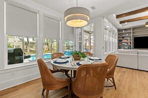 A dining area with a round table, wicker chairs, and a hanging light fixture.