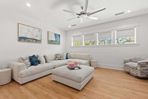 A living room with a sectional sofa, a coffee table, a ceiling fan, and a large window with a view of trees.