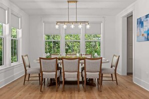 Comedor con una mesa blanca dispuesta para seis personas, rodeada de sillas de madera con asientos acolchados.