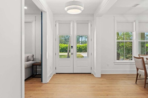 A room with a wooden floor, white walls, a double door with glass panels, and a view of greenery outside.