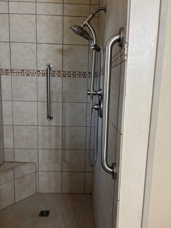 A shower area with a handheld showerhead, a handheld shower attachment, and a grab bar.